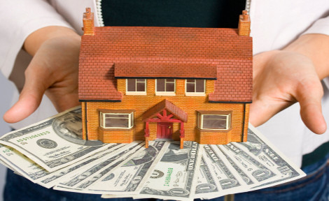 A person holding a miniature house and some dollar bills